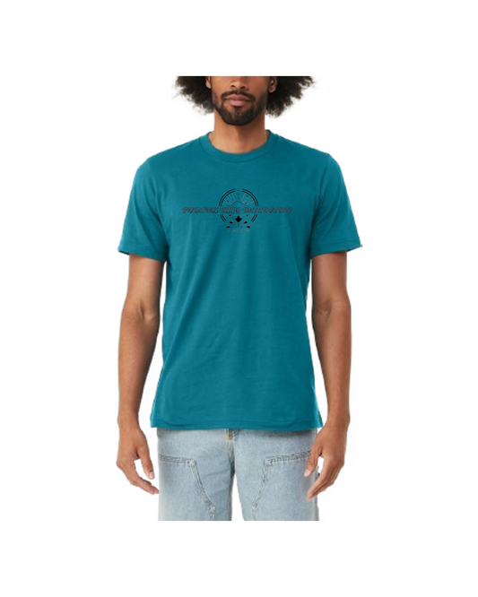 teal shirt with Indigenous Rising logo with We Are Still Here below